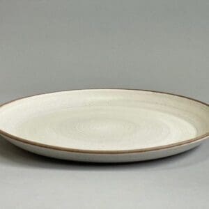 A white plate with brown rim on top of grey surface.