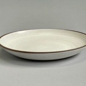 A white plate with brown trim on top of a table.