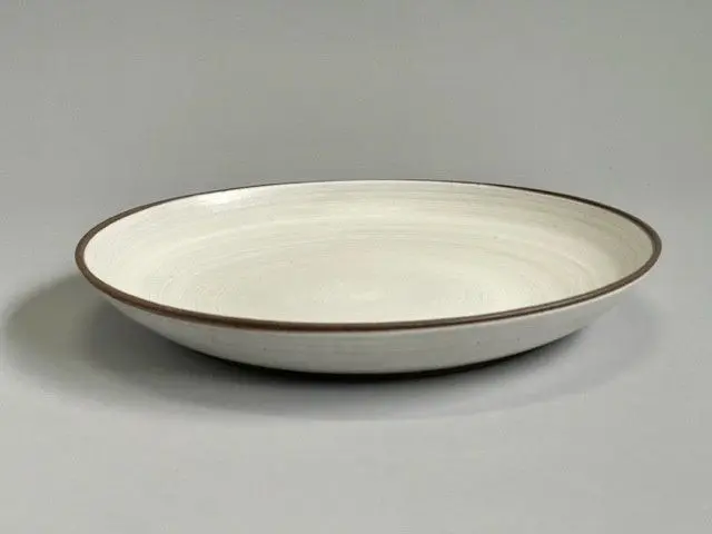 A white plate with brown trim on top of a table.