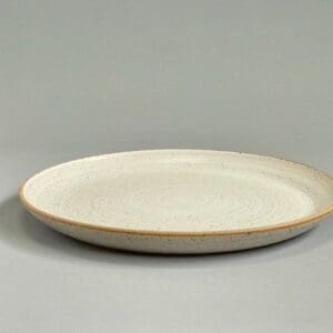 A white plate with brown rim on top of grey surface.
