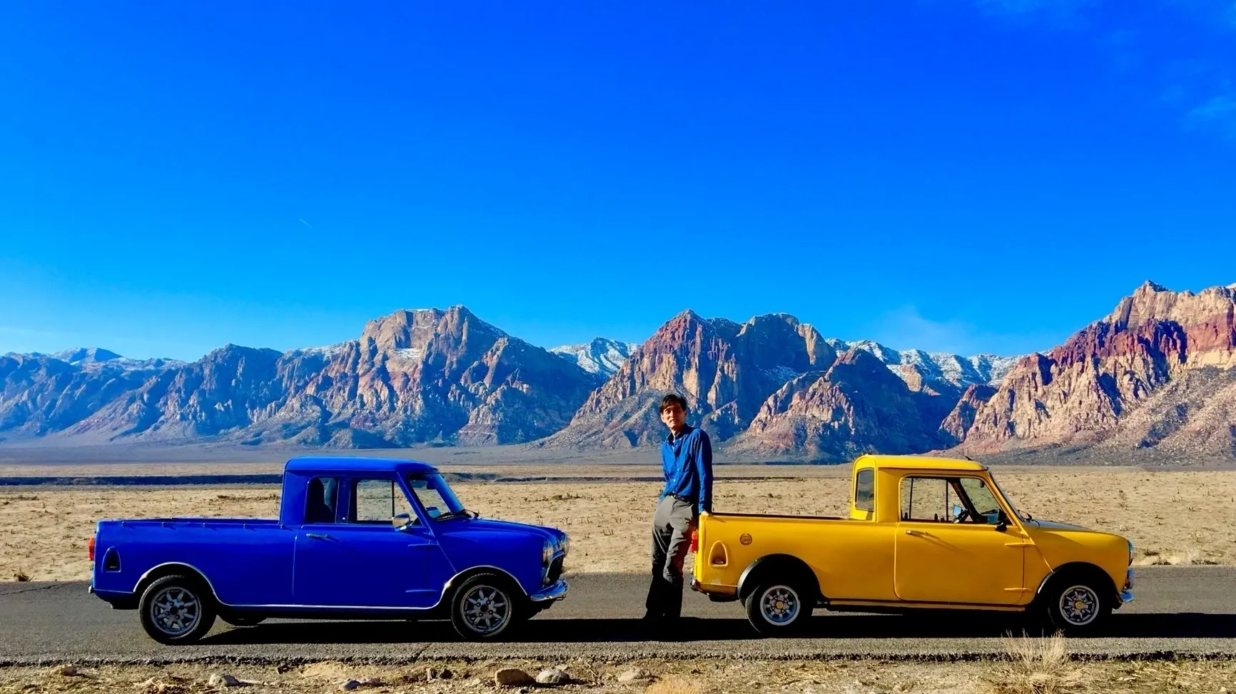 A man standing next to two old trucks.