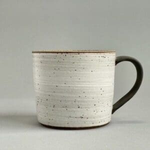 A white cup with black handle and brown rim.