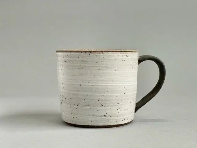 A white cup with black handle and brown rim.