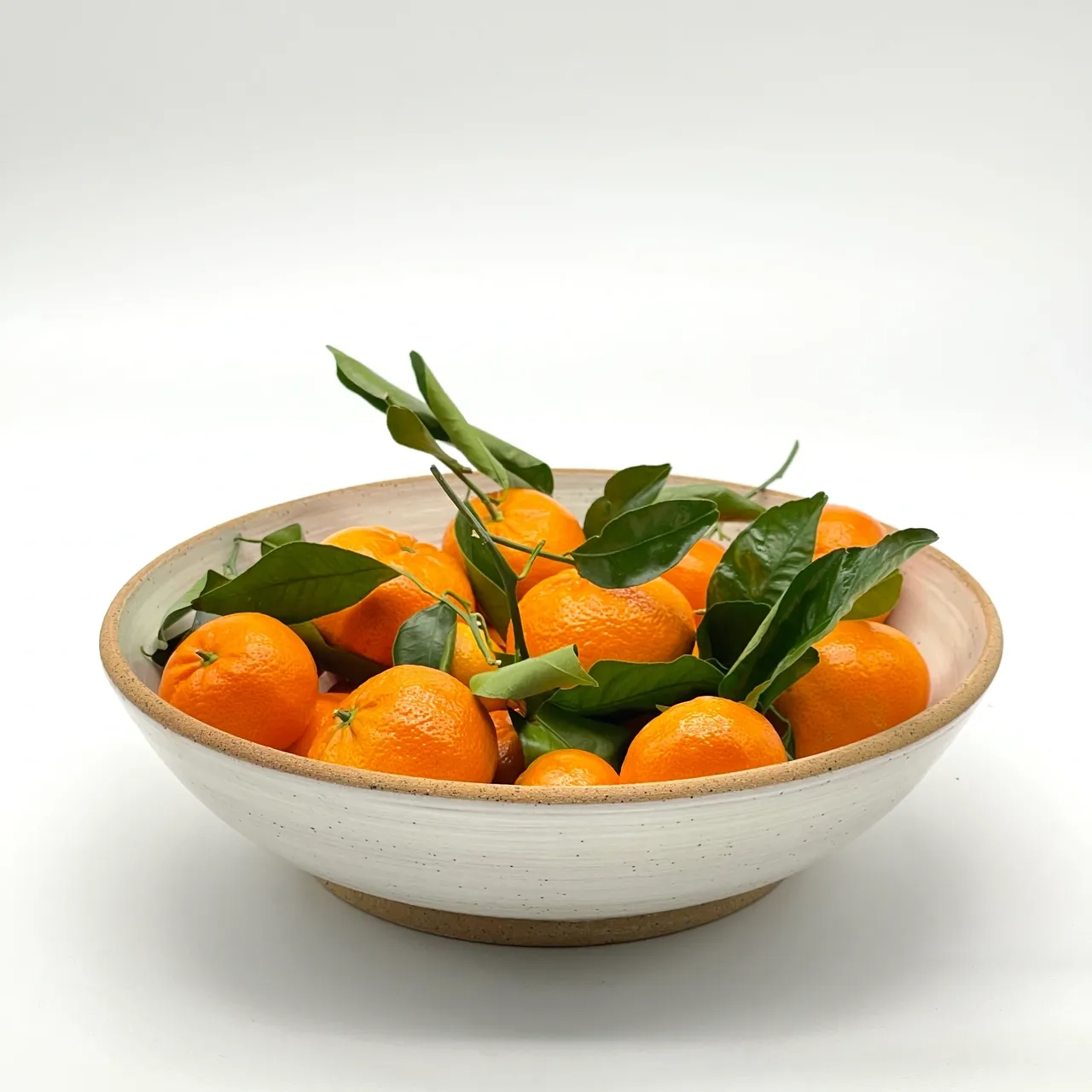 A bowl of oranges with leaves in it.