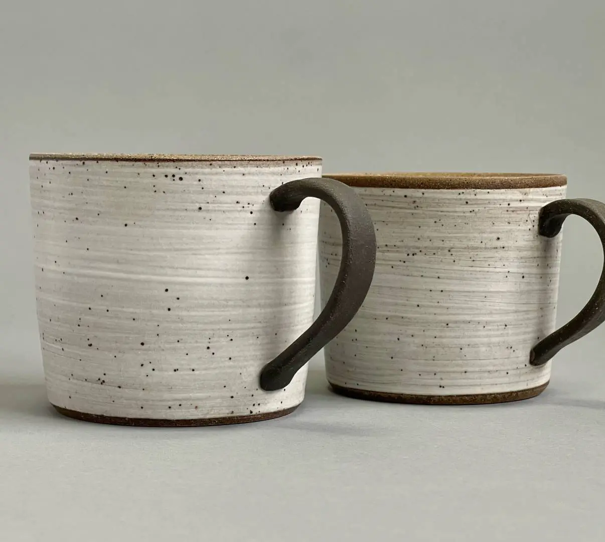 Two cups with handles are sitting on a table.