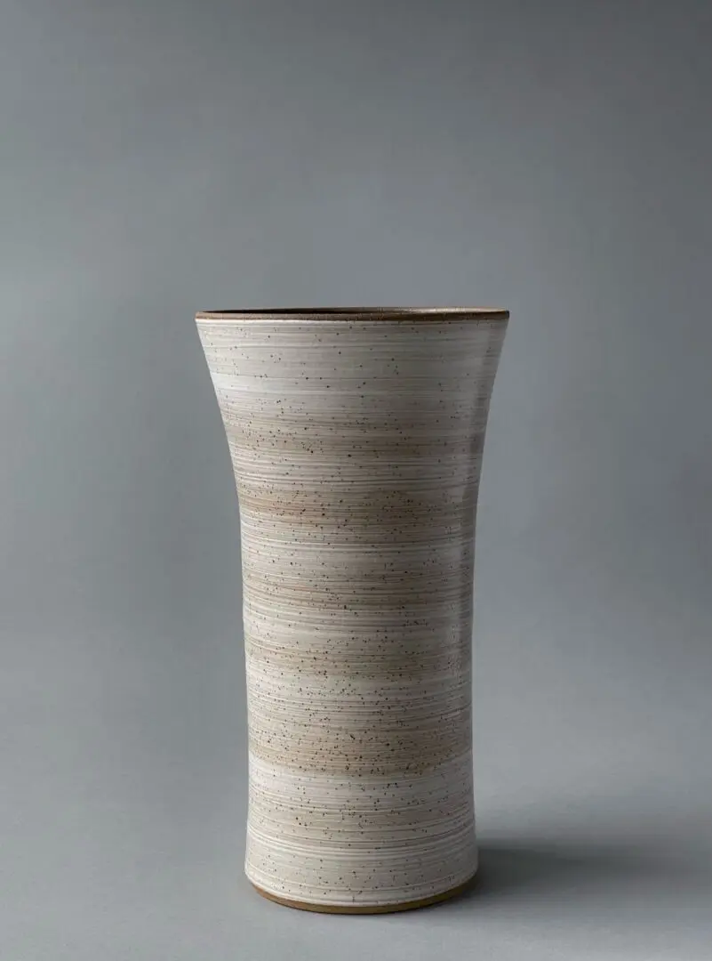 A tall white vase with brown stripes on the bottom.